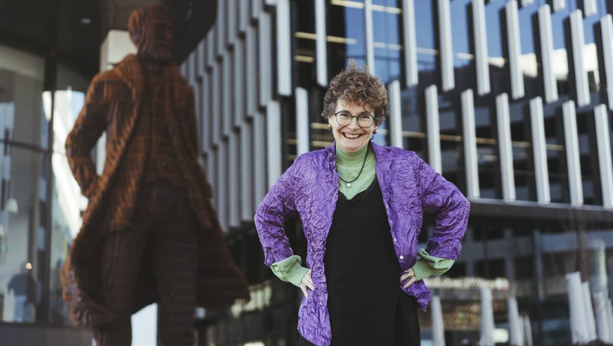 Kim Rubenstein, wearing a light purple jumper and patterned scarf, standing in front of the Andrew Inglis Clark statue